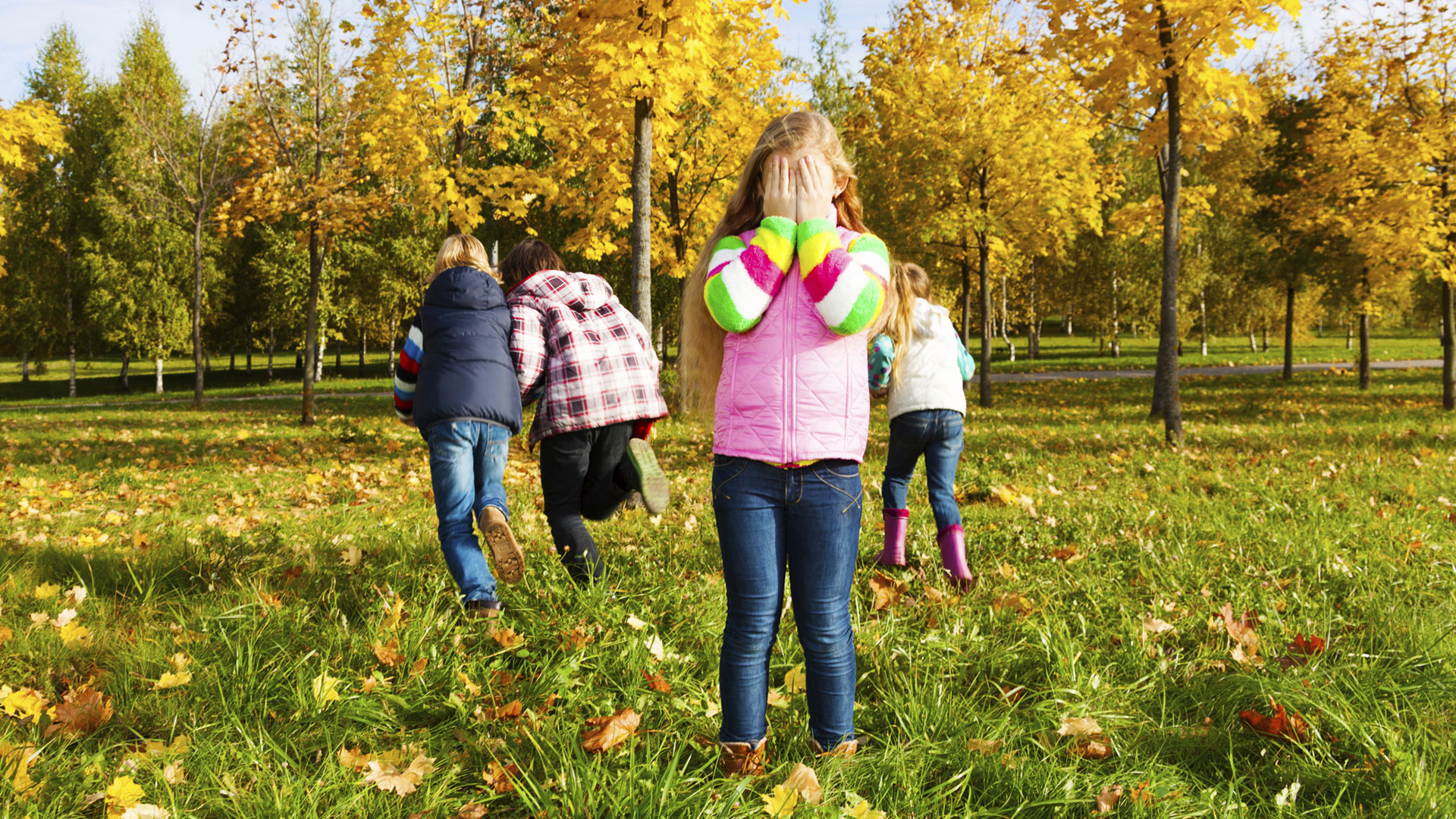 A group of children playing hide-and-seek in a park with bright yellow and orange autumn trees