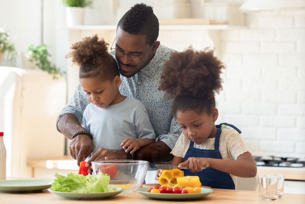 A father and his two young daughters cooking together and dicing colorful vegetables