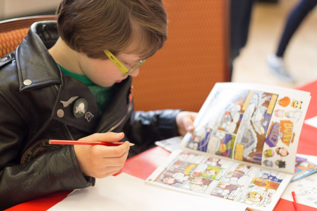A boy with bright green eyeglass frames looking closely at a comic he is holding
